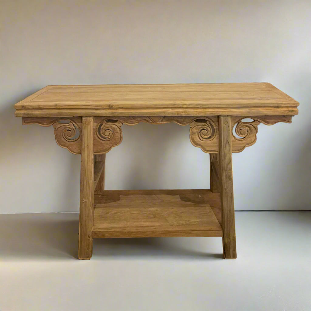 Wooden console table with intricate carvings against a white brick wall.